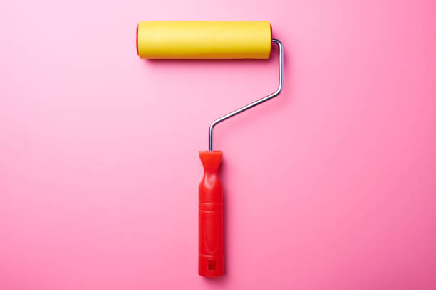 istock Home repair concept. Yellow roller for wallpaper and pink wall with copy space. 1130994583
