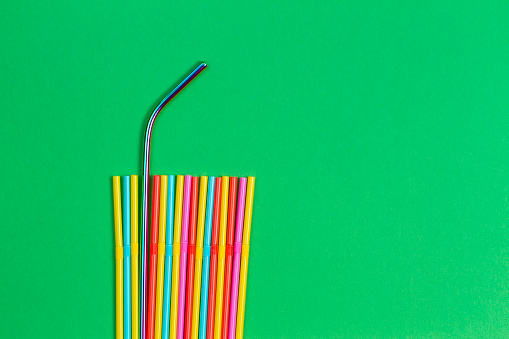 Stainless steel reusable drinking straw with plastic straws on green background.