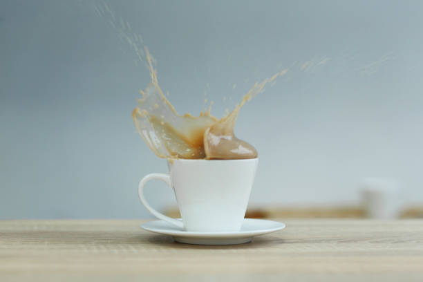 Splash in white cup of coffee on wooden table.