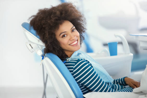 Dental appointment was successful and painless. Closeup side view of a cheerful of mixed race early 30's woman sitting in a dentist chair and smiling to the camera dentists chair stock pictures, royalty-free photos & images