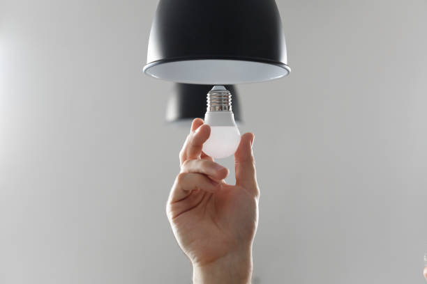 Changing the bulb for led bulb in floor lamp in black colour. On light gray background. Changing the bulb for led bulb in floor lamp in black colour. On light gray background. energy efficient lightbulb stock pictures, royalty-free photos & images