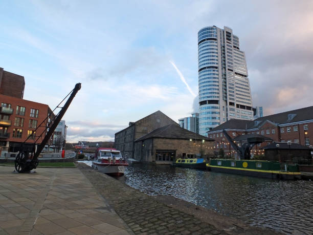 the granary wharf area in leeds with an old crane and boats on the canal with city center buildings and historic waterside achitecture the granary wharf area in leeds with an old crane and boats on the canal with city center buildings and historic waterside achitecture wharfe river photos stock pictures, royalty-free photos & images