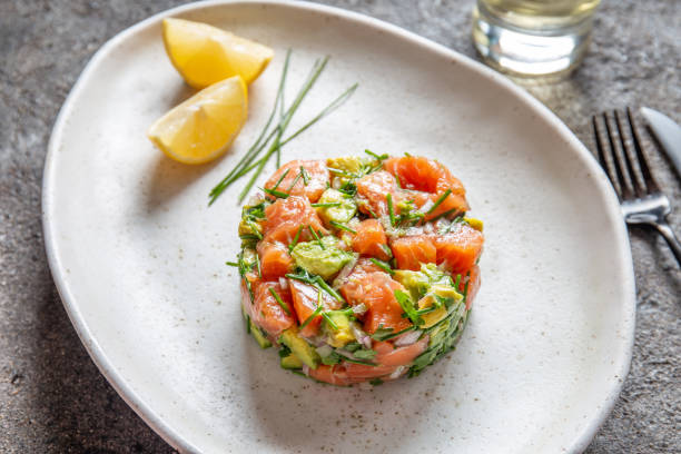 PERUVIAN FOOD. Salmon ceviche with avocado, spring onion and lemon on white plate served with white wine stock photo