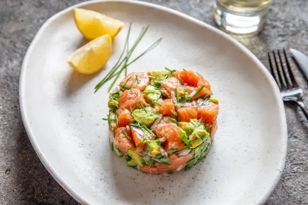 PERUVIAN FOOD. Salmon ceviche with avocado, spring onion and lemon on white plate served with white wine.