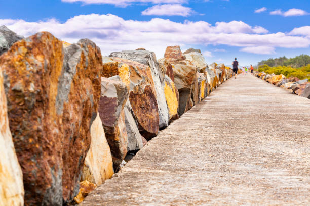 People walking and running on the breakwall at Harrington, NSW, Australia