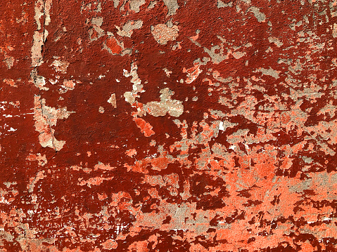 Macro image of an exterior stone wall, with faded and peeled layers of blue, red and white paint in different areas of the surface.
