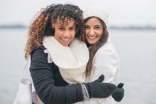 Gorgeous ethnic, female adult friends hug each other while skating on a winter day.