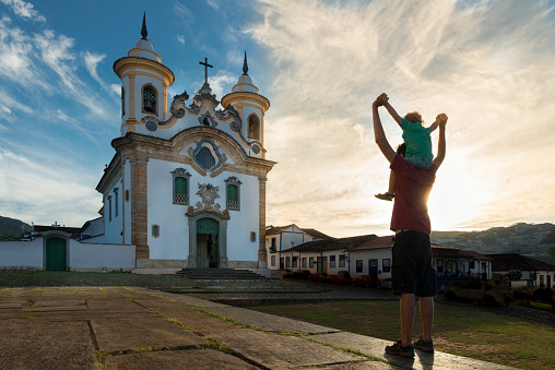 Father carrying son on his shoulders while exploring the town of Mariana and its churches in Minas Gerais, Brazil.