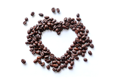 Love of coffee expressed in spilled coffee beans in the shape of a heart isolated on white background