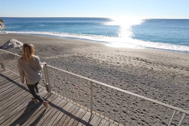 istock Young woman walks down boardwalk along the sea 1131064999