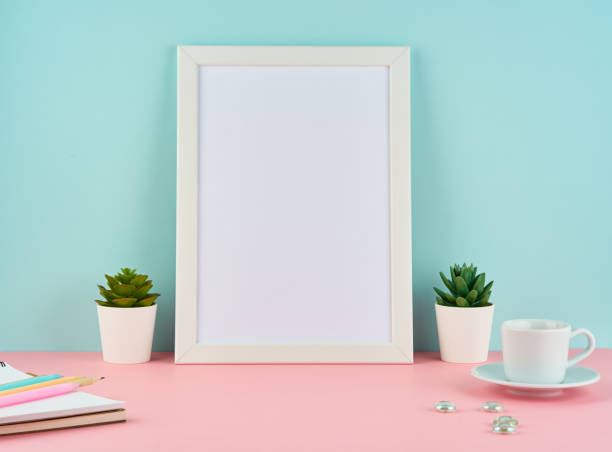 istock Mockup with blank white frame, plant cactus, cup of coffee or tea on pink table against blue wall with copy space. 1131078526