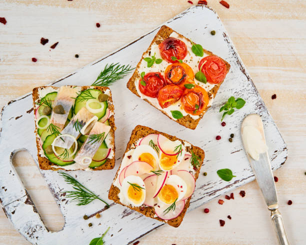 istock Smorrebrod - traditional Danish sandwiches. Black rye bread with herring, egg, tomatoes, radish on white wooden table, top view 1131080679