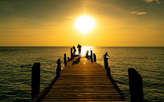 Happy family play together on summer vacation at wooden bridge at sunset. Parent and children playing at the beach on holiday. Paradise tropical sea. Kids having fun with jump to the sea in evening.