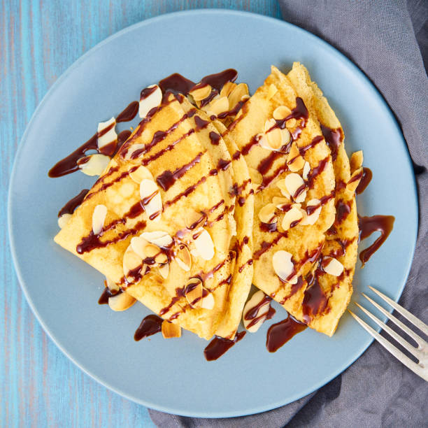 istock Two pancakes with chocolate syrup, almond flakes on plate, honey flows from spoon, top view, macro 1131083009