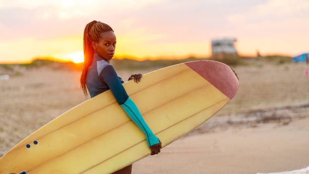 istock African woman holding surfboard and walking on beach 1131083166