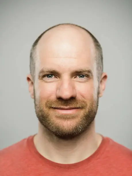 Close up portrait of mature adult adult caucasian man with happy expression looking at camera against white gray background. Vertical shot of canadian real people smiling in studio with short balding read hair and blue eyes. Photography from a DSLR camera. Sharp focus on eyes.