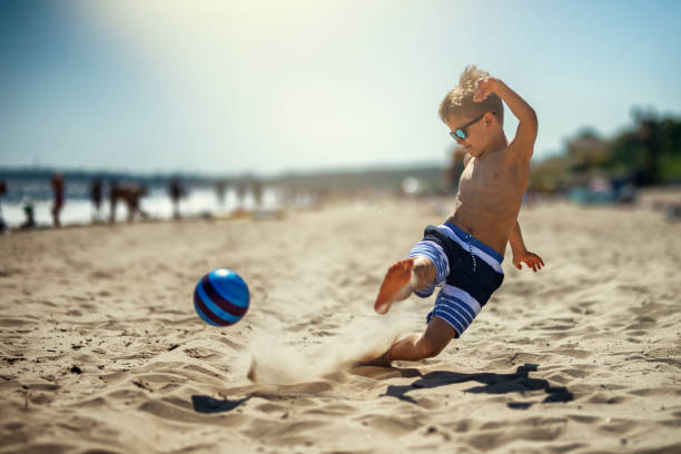 little boy playing soccer on the beach - beach football imagens e fotografias de stock