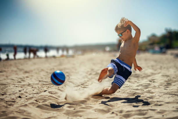 маленький мальчик, играющий в футбол на пляже - soccer child little boys playing стоковые фото и изображения