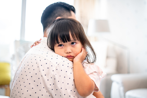Cute Chinese girl crying on her father’s shoulder.
