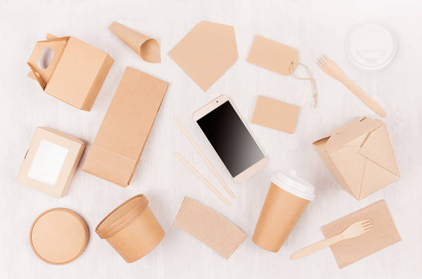 istock Blank different cardboard packaging for fast food - coffee cup, screen phone, cutlery, sugar, spice, container and box for sushi, noodles on white wood board. 1131086364