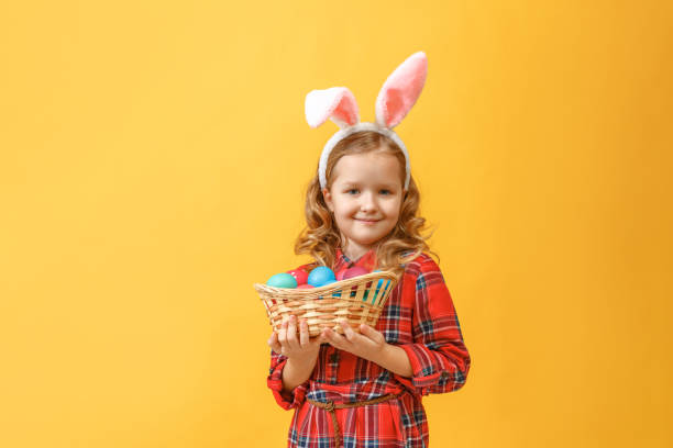 ウサギの耳を持つかわいい子供の女の子は、色付きの背景にイースターエッグのバスケットを保持しています。 - easter egg easter yellow paint ストックフォトと画像
