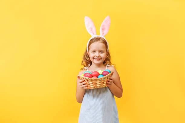 イースターのバスケットを保持しているウサギの耳を持つかわいい子供の女の子 - easter egg easter yellow paint ストックフォトと画像