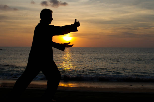 Silhouette of a man practicing Taiji with sunset background at the beach stock photo