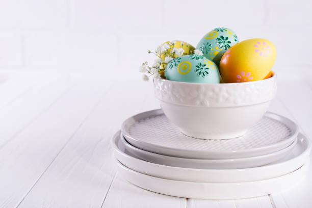 istock Stack of plates and bowl with colorful Easter eggs, spring easter decoration on white wooden table 1131092735