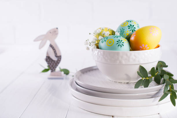 istock Stack of plates and bowl with colorful Easter eggs, spring easter decoration on white wooden table 1131092748