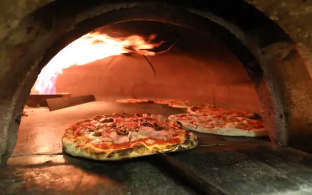 fire and many pizzas inside an oven in the italian pizzeria