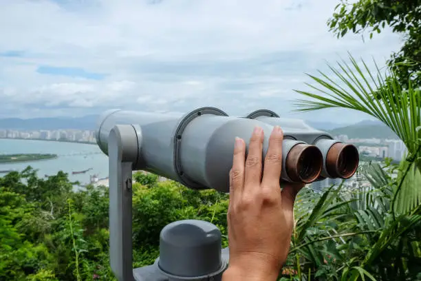 Close up shot of woman hands holding a coin operated binoculars, looking through city view