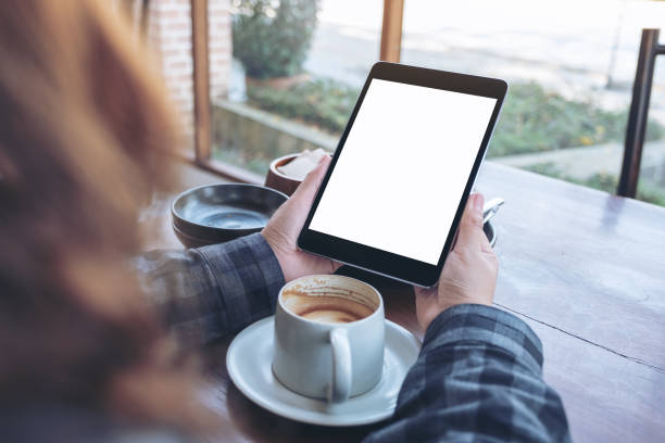 istock Mockup image of woman's hands holding black tablet pc with blank screen with coffee cup on wooden table in cafe 1131102105