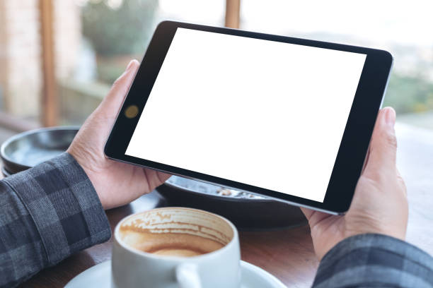 istock Mockup image of woman's hands holding black tablet pc with blank screen with coffee cup on wooden table in cafe 1131102129