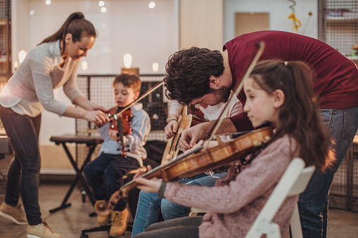 Young man learn how to play violin under instruction of mature woman female professor tutor at home take private class