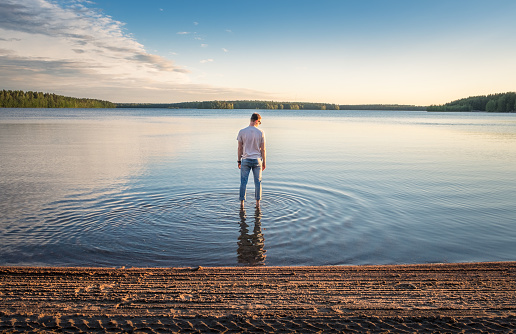 Man standing in water at beautiful summer day with idyllic lake and tranquil evening in Finland