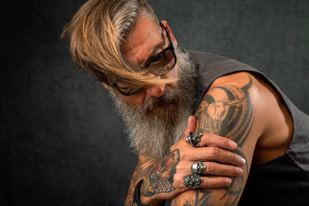 Portrait of a cool biker with a grey beard and sunglasses Portrait of a cool biker with a grey beard and sunglasses shoulder tattoo designs for men stock pictures, royalty-free photos & images