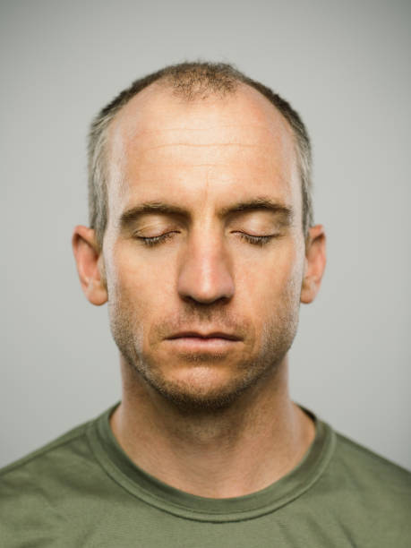Portrait of real caucasian man with blank expression and eyes closed Close up portrait of mid adult caucasian man with blank expression and eyes closed against gray white background. Vertical shot of american real people resting in studio with short balding hair and blue eyes. Photography from a DSLR camera. Sharp focus on eyes. eyes closed stock pictures, royalty-free photos & images
