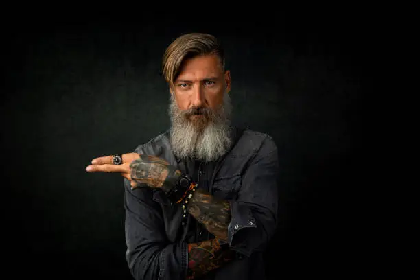 Portrait of a bearded hipster, who is pointing with his fingers to something, isolated on a black background