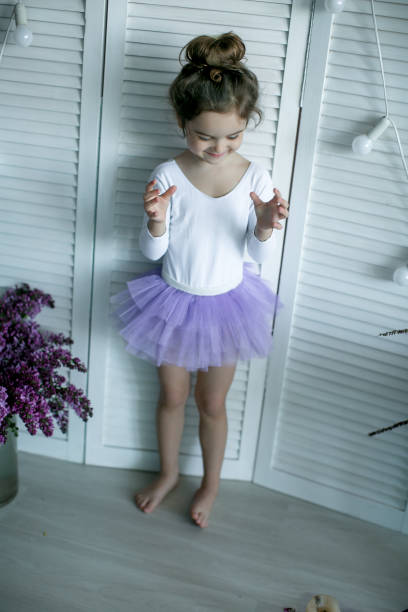 entzückendes kleines mädchen, das als ballerina in einem tutu gekleidet ist, ihre ballettschuhe einbindet. - ballet dress studio shot costume stock-fotos und bilder