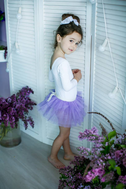 entzückendes kleines mädchen, das als ballerina in einem tutu gekleidet ist, ihre ballettschuhe einbindet. - ballet dress studio shot costume stock-fotos und bilder