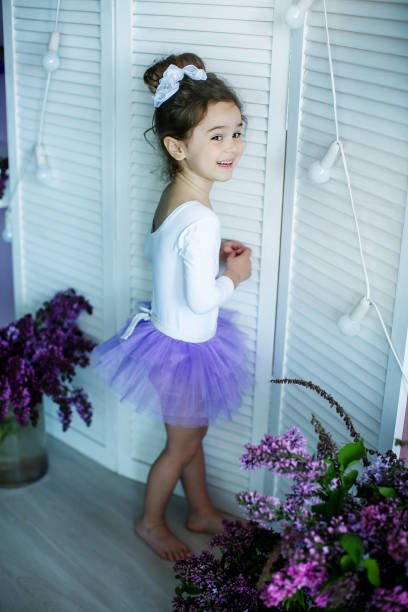 entzückendes kleines mädchen, das als ballerina in einem tutu gekleidet ist, ihre ballettschuhe einbindet. - ballet dress studio shot costume stock-fotos und bilder