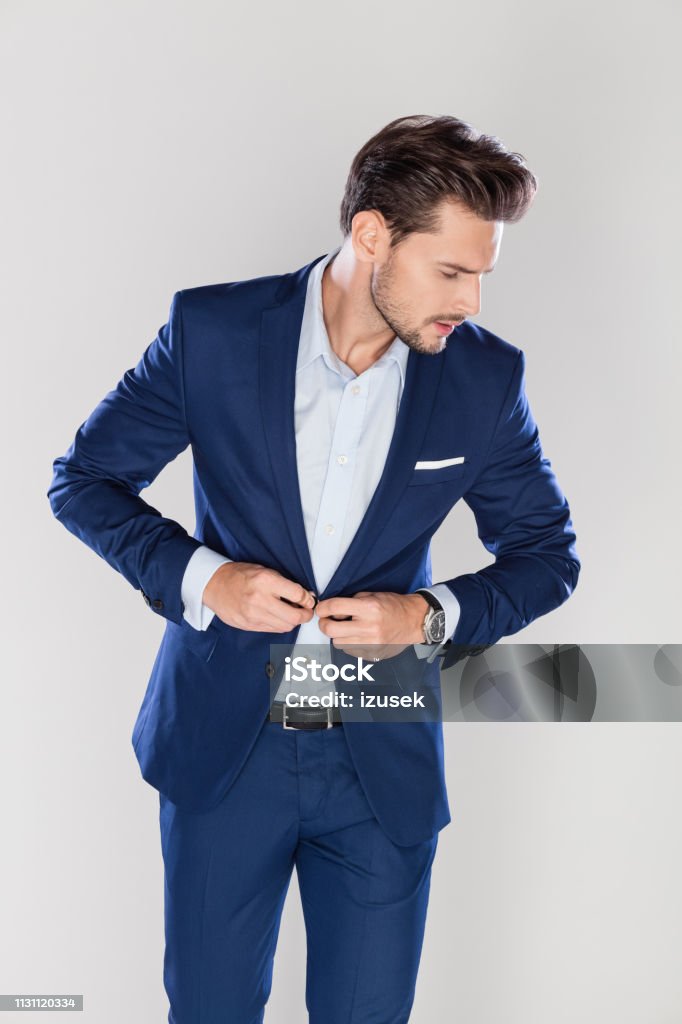 Handsome businessman buttoning his jacket Portrait of handsome young businessman buttoning his jacket while standing on gray background Men Stock Photo