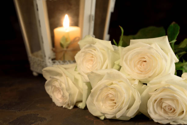 Beautiful white roses and candle on table against black background. Beautiful white roses and candle on table against black background. Funeral symbol rose bouquet red table stock pictures, royalty-free photos & images