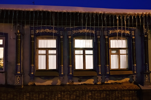Russian traditional architecture at winter. Facade of the house with three luminous windows with carved platbands at night. Voronezh, Russia