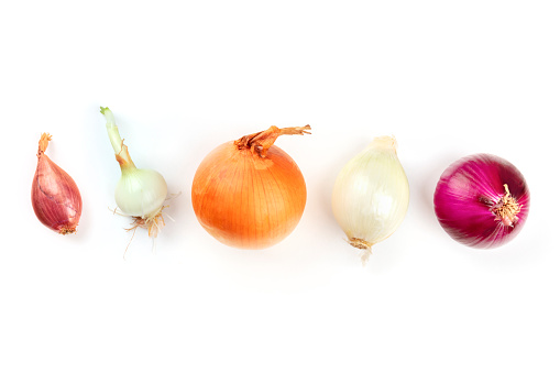 An assortment of various types of onions, shot from the top on a white background with copy space