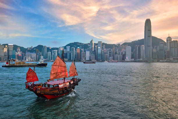 Junk boat in Hong Kong Victoria Harbour Hong Kong skyline cityscape downtown skyscrapers over Victoria Harbour in the evening with junk tourist ferry boat on sunset with dramatic sky. Hong Kong, China junk bay hong kong stock pictures, royalty-free photos & images