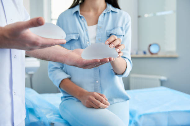 Woman receiving consultation of plastic surgeon at the clinic Doctor holding in his hands two silicone implants. Female patient trying to touch them breast photos stock pictures, royalty-free photos & images
