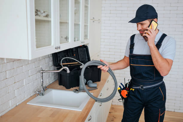 istock Young plumber talking on phone in kitchen at sink. He hold hose. Reparing. Toolbox on desk. Daylight. 1131133072