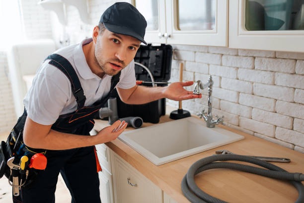 istock Amazed young man look on caerma and point on sink in kitchen. Worker has hose and toolbox on desk. Guy wear uniform. 1131133075