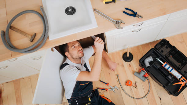 istock Young plumber look under sink in kitchen. He put new hose. Tools with opened box on floor. Hose and wrench with nippers on desk. 1131133098